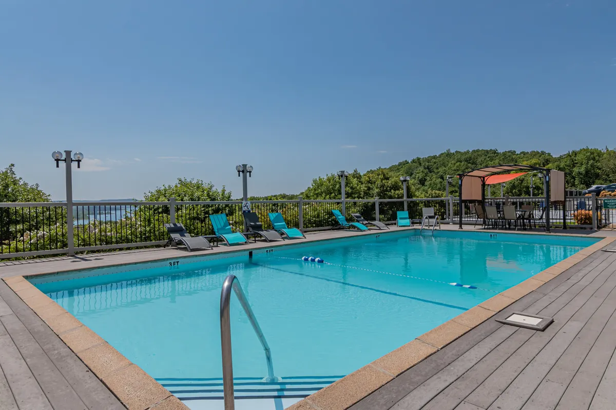 This image features a sparkling outdoor swimming pool surrounded by comfortable lounge chairs and a shaded canopy area, all set against a lush backdrop of greenery. The tranquil, inviting setting showcases leisure activities like swimming, sunbathing, and relaxed social gatherings by the pool.