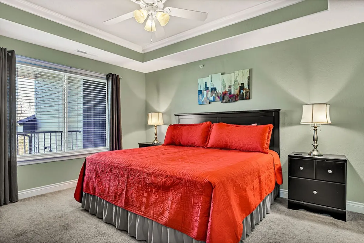 A cozy, inviting master bedroom featuring a red bedspread, tasteful artwork above the bed, and nightstands with warm-lit lamps flanking each side. The room exudes comfort and relaxation, ideal for unwinding after a busy day.