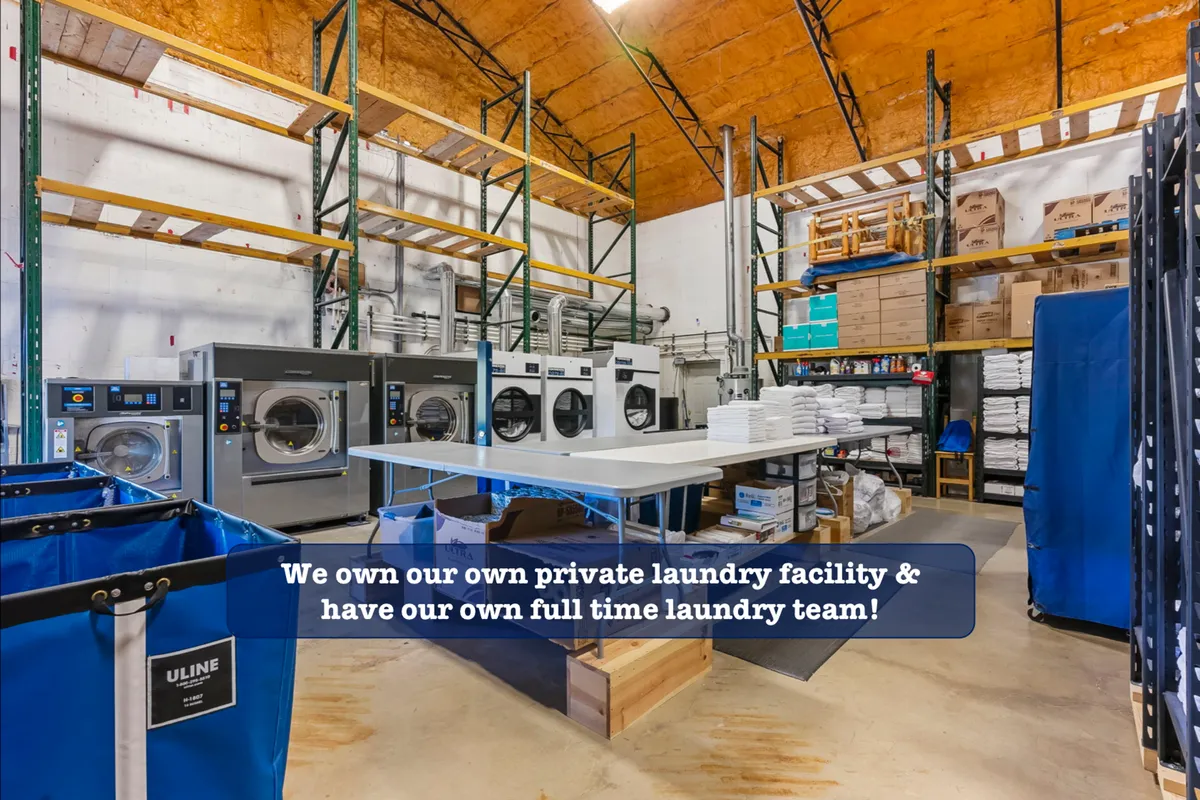 An interior view of a professional laundry facility featuring industrial washing machines, organized storage shelves, and a designated laundry folding area. The scene exudes a sense of efficiency, cleanliness, and operational professionalism.