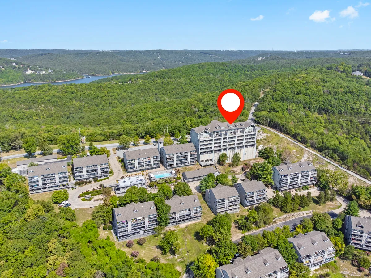 This exterior shot captures the large residential buildings of the resort complex, framed by green landscaping, scenic wooded trails, and a glimpse of the nearby pool area. Roadways and pathways leading into the property further emphasize accessibility and exploration opportunities within the resort grounds.