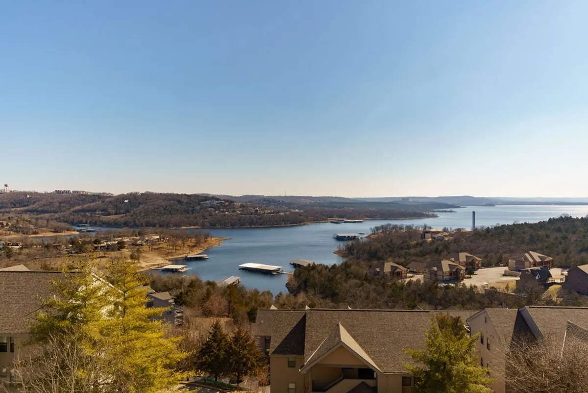 A sweeping, tranquil view of Table Rock Lake surrounded by hills, houses, and lush trees. The scene evokes a sense of peace and natural beauty, with the lake stretching out toward the horizon—ideal for fishing, boating, or simply relaxing as the sun sets.
